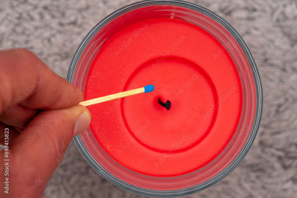 red wax candle with blue headed matchstick approaching the wick. red wax candle with blue headed matchstick approaching the wick.