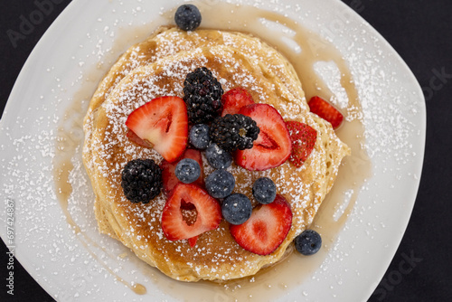 Stack of pancakes on a plate with fresh blueberries and strawberries
