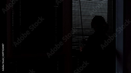 Silhouette of a woman opening the blinds. Wooden blinds that open on large windows in the interior. photo
