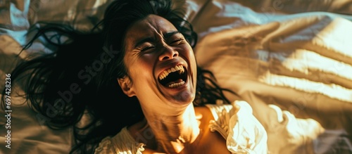 An Asian woman on the bed, laughing uncontrollably with great joy, doubled over and couldn't stop.