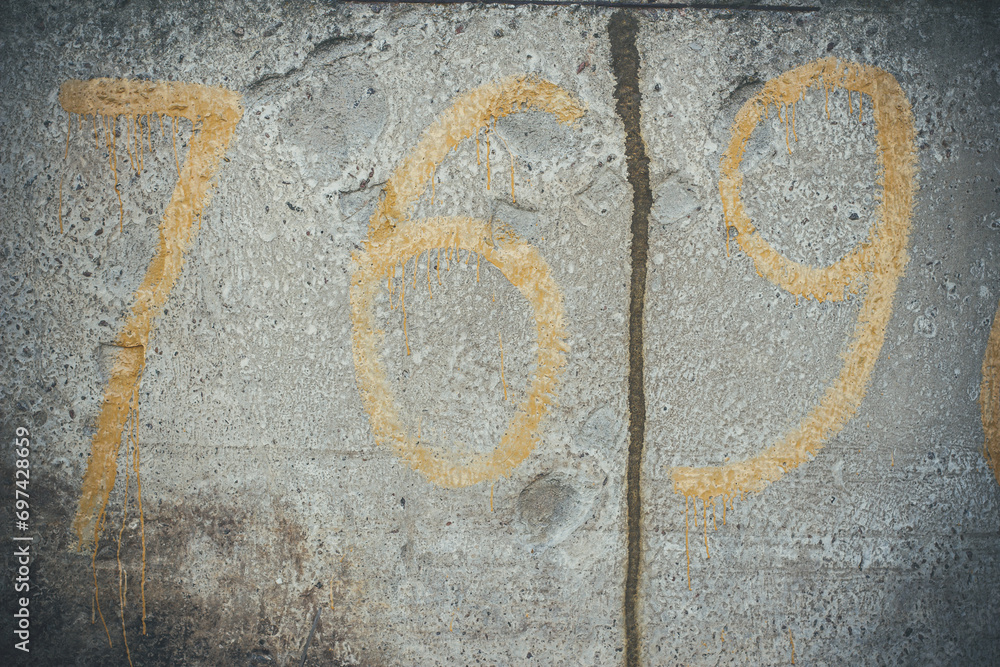 Yellow numbers on a concrete wall, number 7, 6, 9