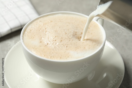 Pouring milk into cup of coffee on grey table, closeup