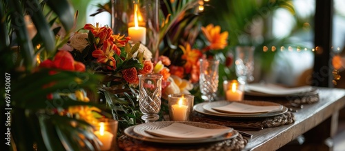 Tropical-style table setting for two people at a festive event decorated with flowers, candles, and leaves. Romantic dinner in a restaurant, wedding, or party with a midsummer mood. Florist decorator