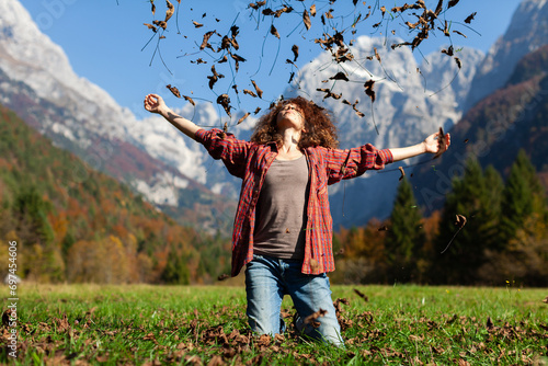 Cheerful Young Woman Kneeling on Meadow and Enjoy Throwing Autumn Leafs in Air on a Beautiful Mountains  Background