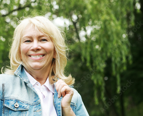 Beautiful blonde woman in a denim jacket in a spring park. Elderly happy lady pensioner. Close up.