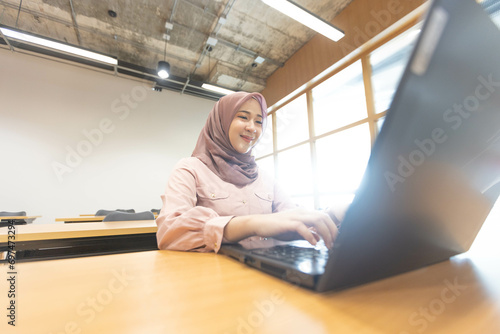 Asian Muslim woman wearing hijab working at office with documents on table, planning to analyze financial report, business plan, investing, financial concept and having fun at work photo