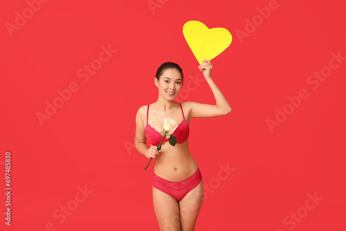 Beautiful young happy Asian woman in sexy underwear with paper heart and white rose on red background. Valentine's Day celebration