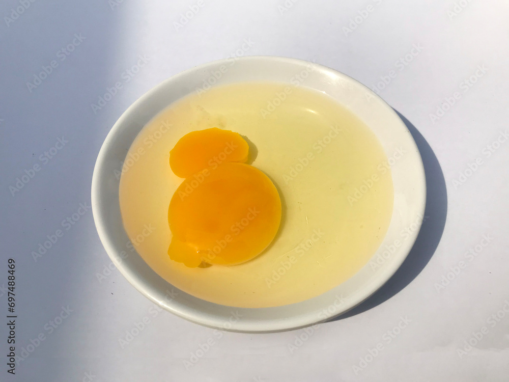 Broken chicken egg yolk on a white saucer on a white background. Broken chicken egg yolk on a white saucer on a white background.
