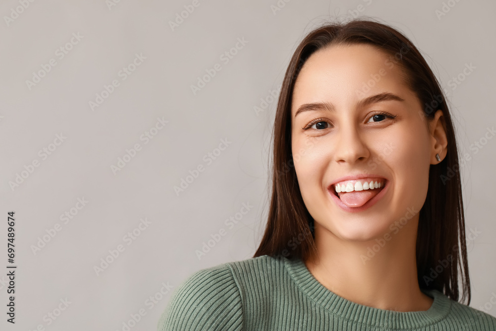 Beautiful young woman showing clean tongue on grey background Beautiful young woman showing clean tongue on grey background