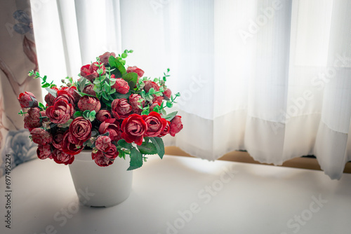 Roses in a vase on a table next to a window lined with white curtains