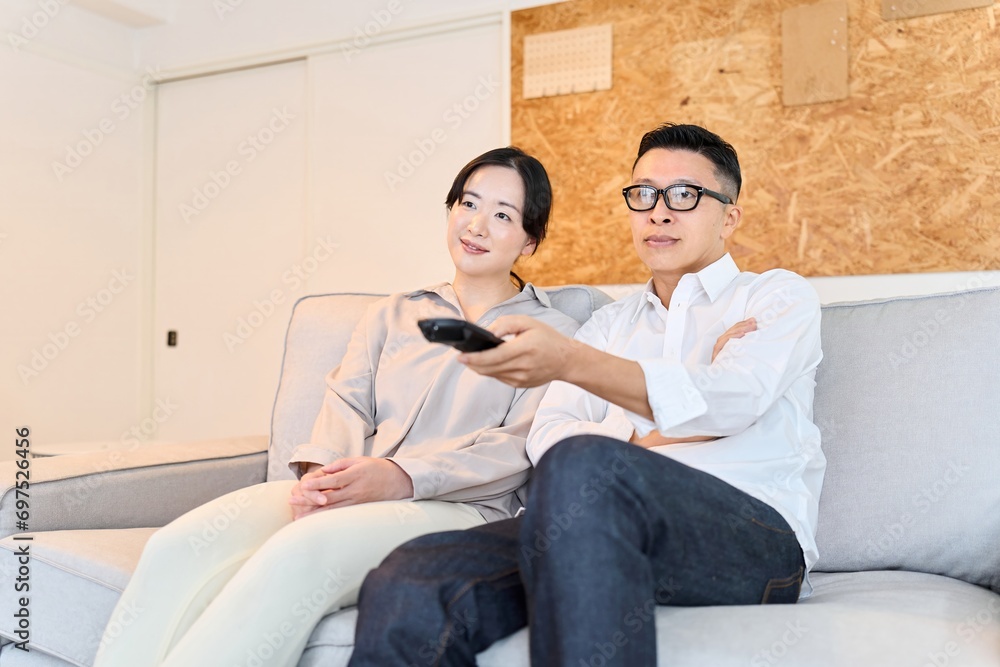Fototapeta premium リビングでテレビを見るアジア人夫婦