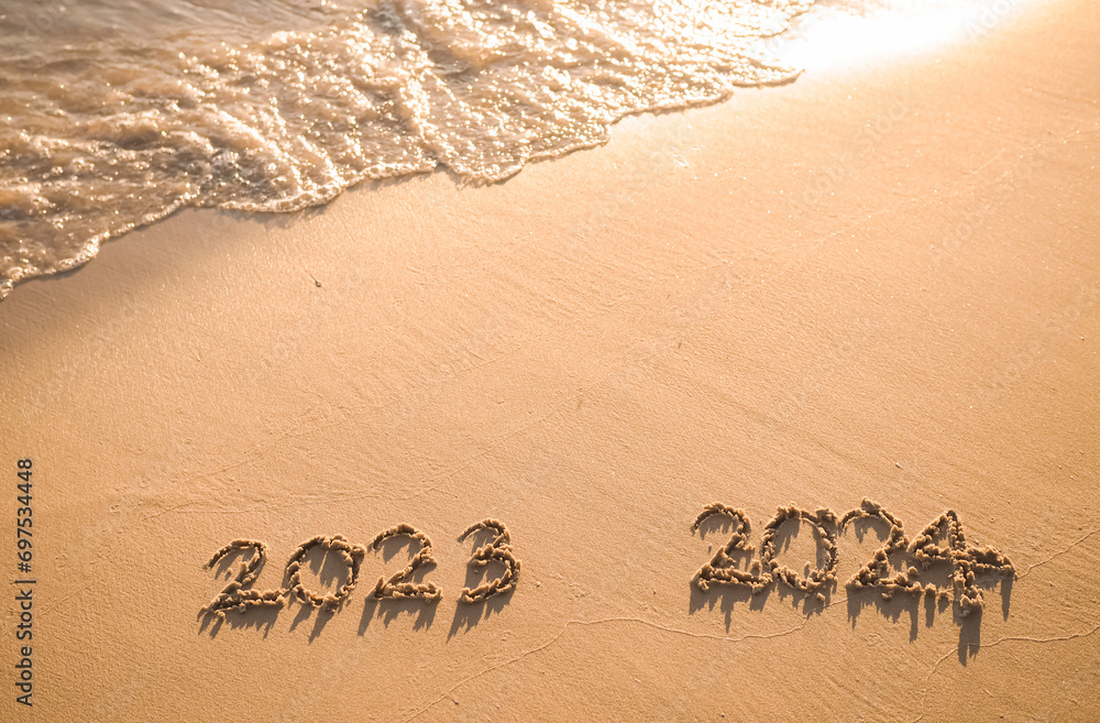 Fototapeta premium Handwritten inscription 2023 and 2024 on the beach in the sunset time. The concept of Goodbye 2023 and Happy New Year 2024
