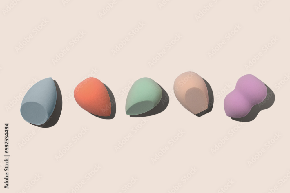 Set of colourful pastel blue, orange, biege, green and purple sponges for makeup on beige background with dark shadows. Beauty blender with different shape.  - obrazy, fototapety, plakaty 