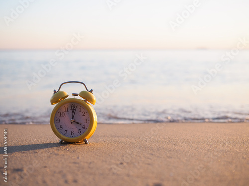 Fototapeta Naklejka Na Ścianę i Meble -  Yellow alarm clock on the beach in the sunset time. The concept about Time to summer, Travel, Vacation and Relaxation