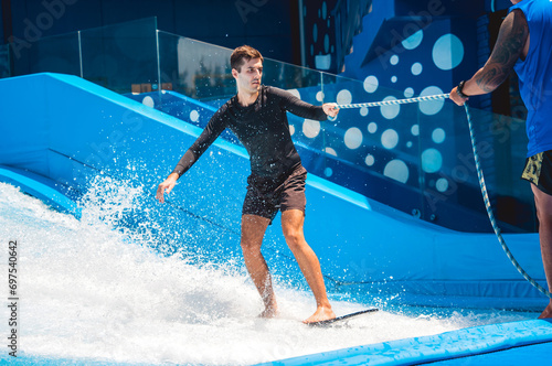 Young man surfing with trainer on a wave simulator at a water amusement park © romaset