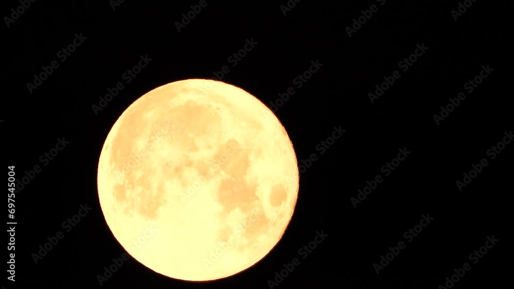 A glowing golden huge full moon seen from earth through the atmosphere against a starry night sky. A large full moon moves across the sky, the moon moving from the left frame to the right. A glowing golden huge full moon seen from earth through the atmosphere against a starry night sky. A large full moon moves across the sky, the moon moving from the left frame to the right.