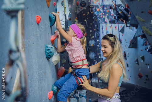 A strong baby climber climbs an artificial wall with colorful grips and ropes.