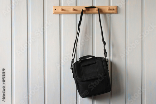 A black camera bag hangs on a wooden white board wall in the room. copy the space.