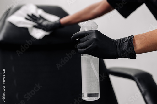 A woman wearing black medical gloves wipes the patient's receiving area with an antibacterial agent. The concept of cleanliness, disinfectants and hygiene in the cosmetologist or dentist office
