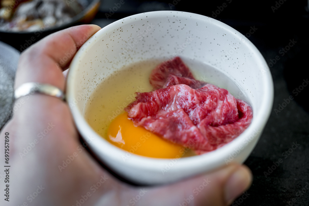 Man holding a white bowl premium fresh beef put in raw yolk egg for boiled Japanese Sukiyaki Man holding a white bowl premium fresh beef put in raw yolk egg for boiled Japanese Sukiyaki