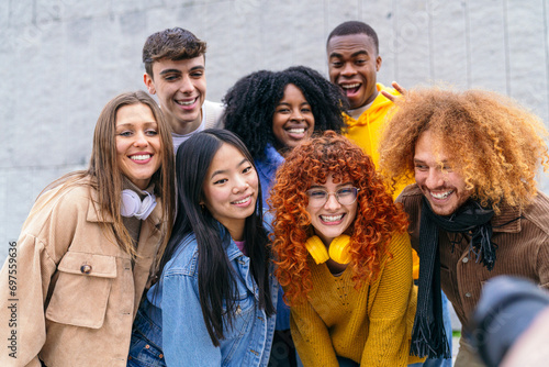 Vibrant multiethnic group of friends posing for a photographer outdoors  exuding joy and friendship against a neutral backdrop.