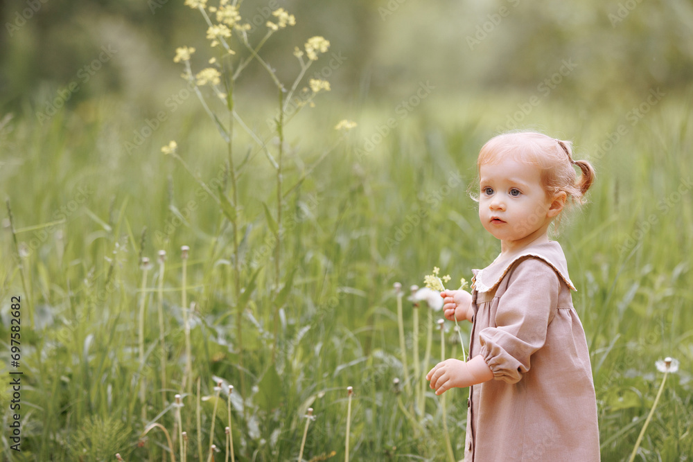 A child in a light brown dress stands in a field, holding a small flower. Surrounded by greenery, the scene captures a moment of innocence and serenity. Concept: Nature, childhood. A child in a light brown dress stands in a field, holding a small flower. Surrounded by greenery, the scene captures a moment of innocence and serenity. Concept: Nature, childhood.