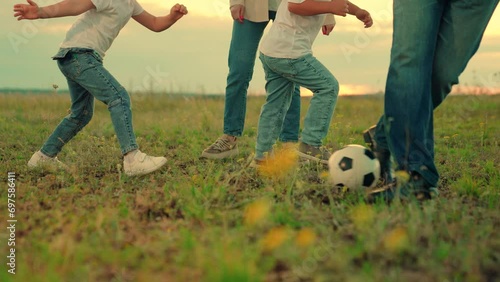 Family have fun playing soccer ball on lawn in park. Young family sport soccer team playing outdoors. Happy family playing football. Child kicks ball. Mom dad child play together, teamwork. Weekend photo