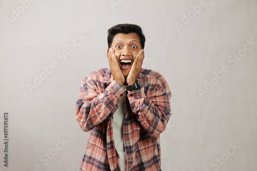 Shocked young Asian man with both hands on cheeks, wow my goodness and amazed facial expression isolated on white background