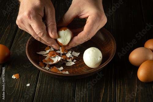 A cook peels a boiled egg from its shell on the kitchen table with his hands. Healthy eggs white diet concept. Advertising space. photo