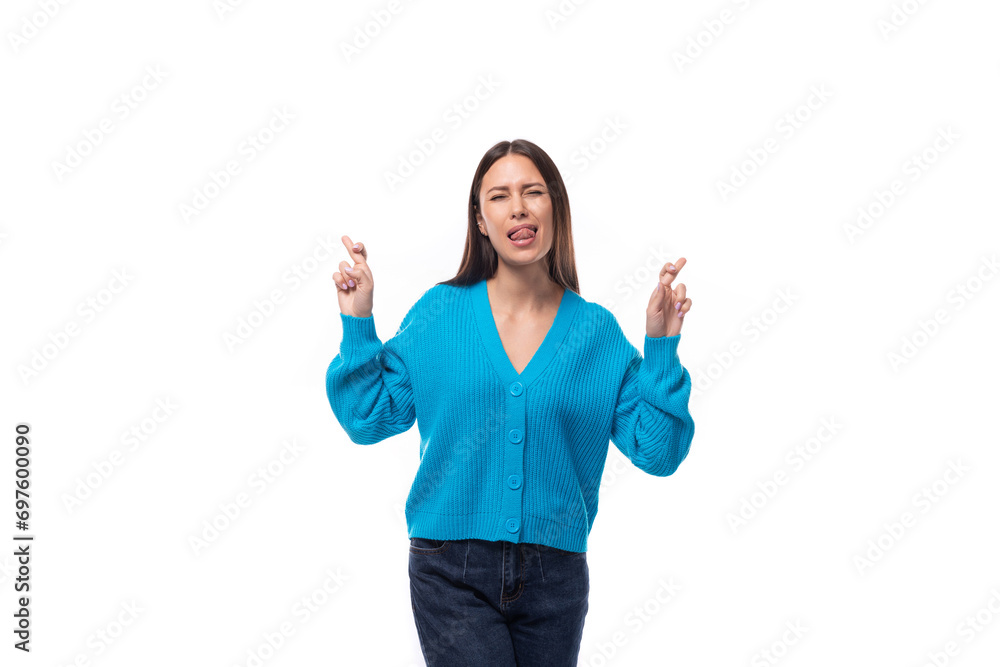 young pretty brunette woman dressed in a blue cardigan crossed her fingers on a white background with copy space young pretty brunette woman dressed in a blue cardigan crossed her fingers on a white background with copy space