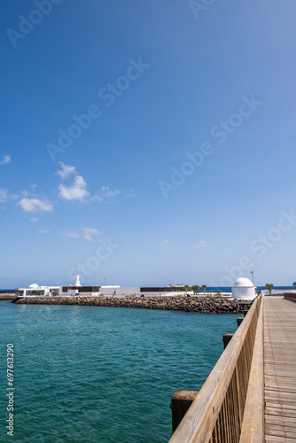 Fototapeta Naklejka Na Ścianę i Meble -  View of the Fermina islet and wooden access bridge. Turquoise blue water. Sky with big white clouds. Seascape. Lanzarote, Canary Islands, Spain.
