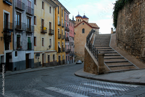 Photo of a street view of the historic center of Cuenca with colorful houses, stairs and a church in the background in the Castilla-La Mancha region, Spain