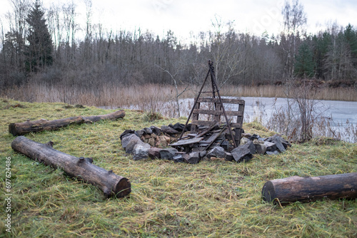 camp fire place with rocks around it nead pond. Tripod for cooking. Oak trunks without bark as chairs. photo