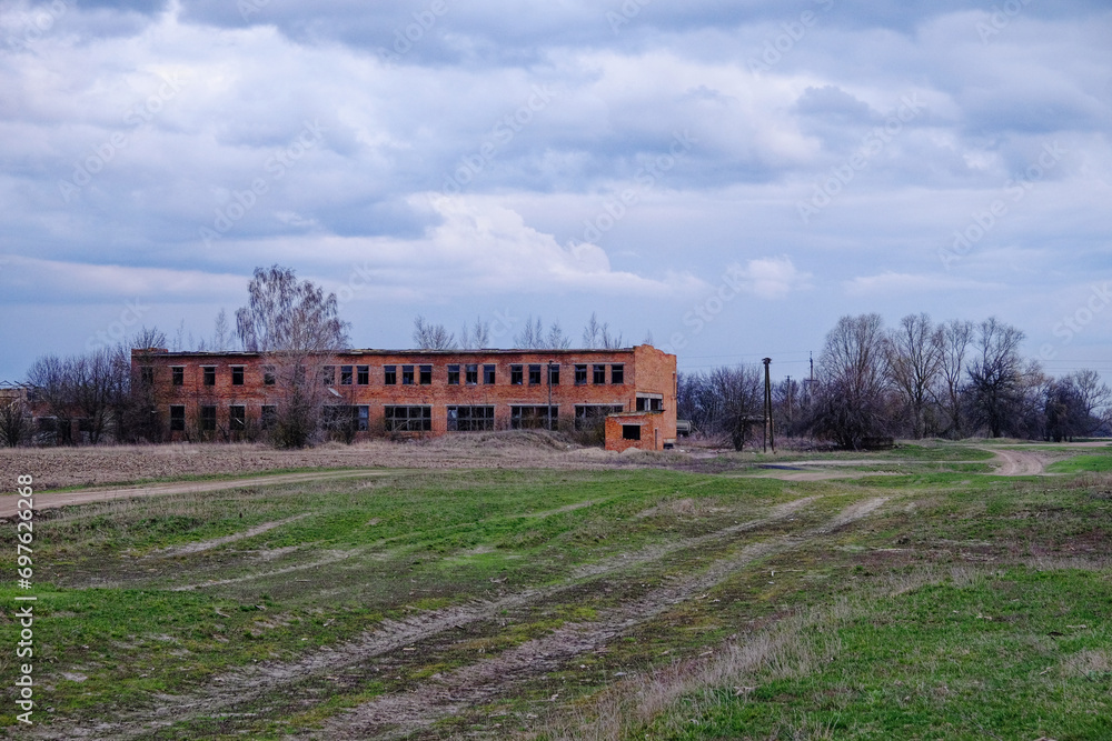 An abandoned brick building, surrounded by wild grass, under a gloomy sky.