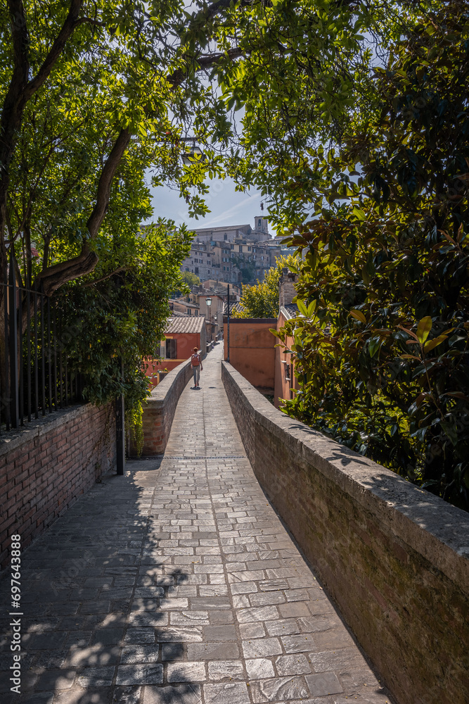 Narrow street with trees between small old brick houses in ancient italian town, Perugia, Italy
