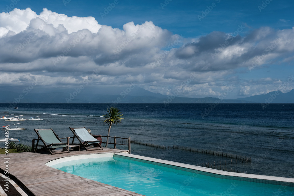 Two lounge chairs by seaside swimming pool on sunny day. Nusa Penida, Indonesia. Two lounge chairs by seaside swimming pool on sunny day. Nusa Penida, Indonesia.