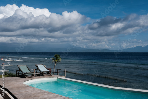 Two lounge chairs by seaside swimming pool on sunny day. Nusa Penida, Indonesia.