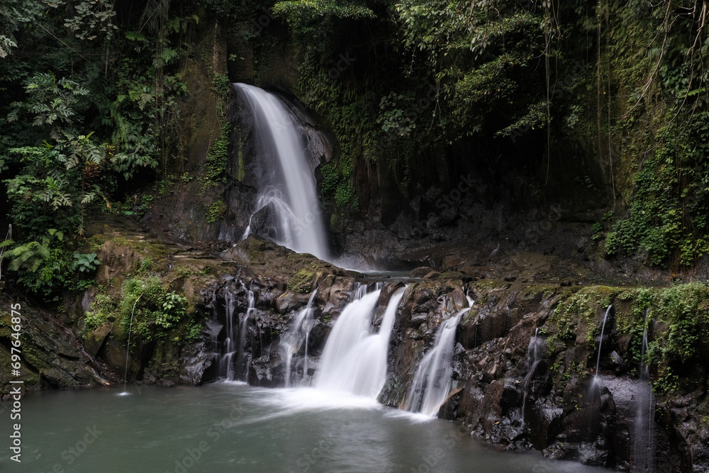 Obraz premium Long exposure shot of Taman Sari waterfall on cloudy day. Bali, Indonesia.
