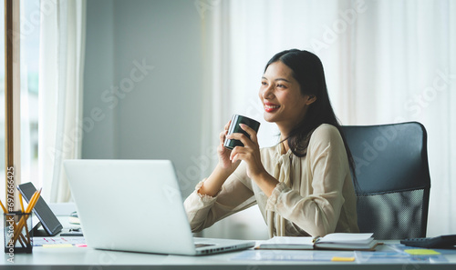 Attractive young businesswoman drinking coffee and working at modern office.