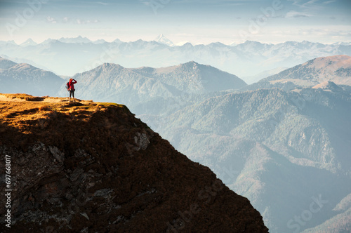 Tourist Hiker in red Jacket Standing on the Border of a Mountain Cliff Admiring the View © Fotopogledi
