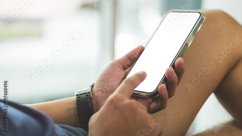 Cropped image of man lying on couch and using mobile phone. White blank screen for your advertise design.