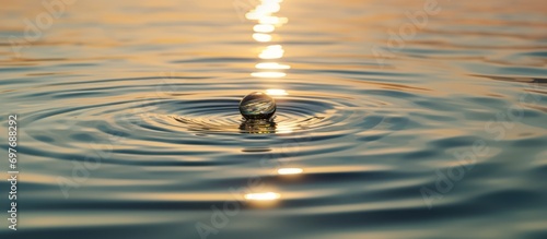 One Water drop Down on a wide calm Sea with ripples at sunset