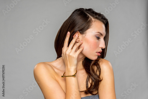 Young alluring brunette beautiful gorgeous female fashion model wearing jewelry on plain grey background isolated 8k
