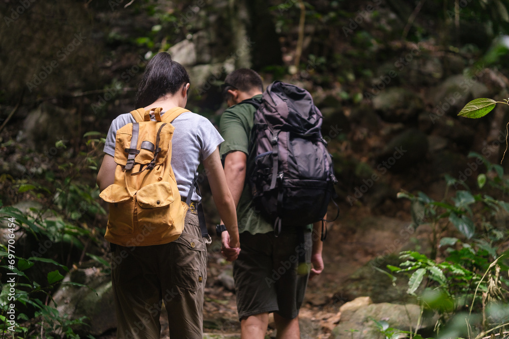 Rear view of young couple trekkers with backpacks walking through the forest. Travel, vacation and active lifestyle concept.