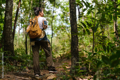 Active female backpacker walking on path in green forest with light sunlight through trees.