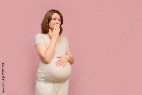 A shy pregnant woman on a pink studio background. Pregnancy of a shame woman with a belly, copy space