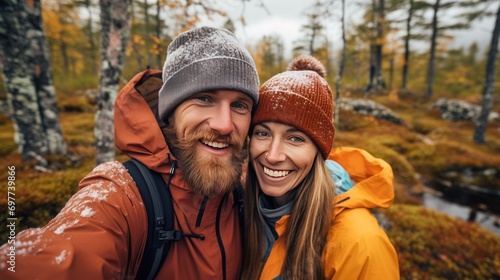 Happy couple of hikers taking a selfie in the autumn forest. They are wearing warm clothes.