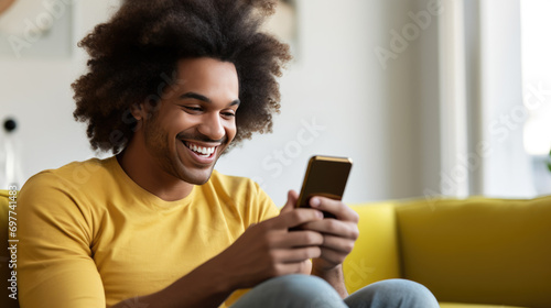 Wallpaper Mural Smiling man sits on the sofa at home and holding his smartphone in his hands Torontodigital.ca