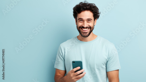 Young man smiling and holding his smartphone on a colored background photo