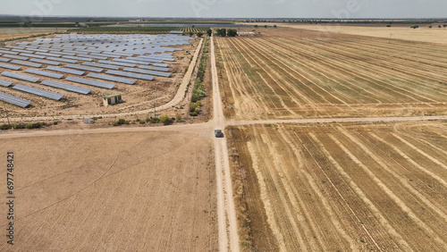 Aerial view of a car driving on dirt roads between large expanses of crop fields and photovoltaic plants photo